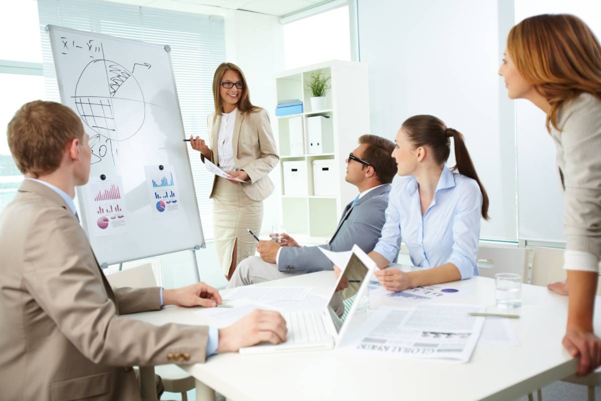 Woman in front of whiteboard talking to people around a white table