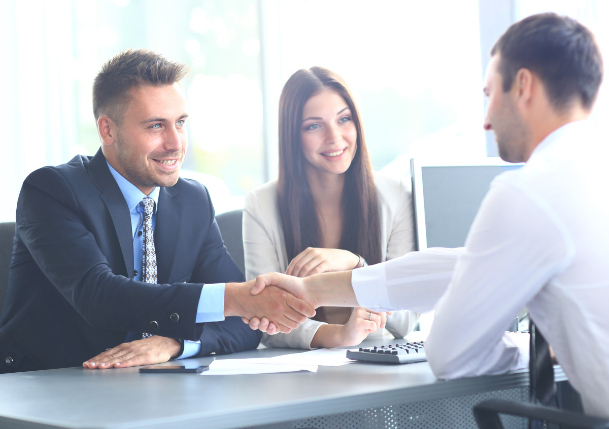 A couple sitting and with man handshaking hands with man across the table