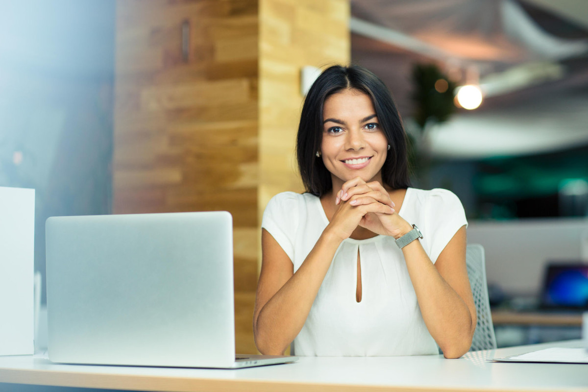 A brunette woman wearing a white shirt and a watch smiling at the camera