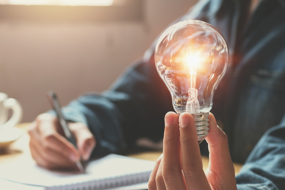 A person writing and holding a lit light bulb