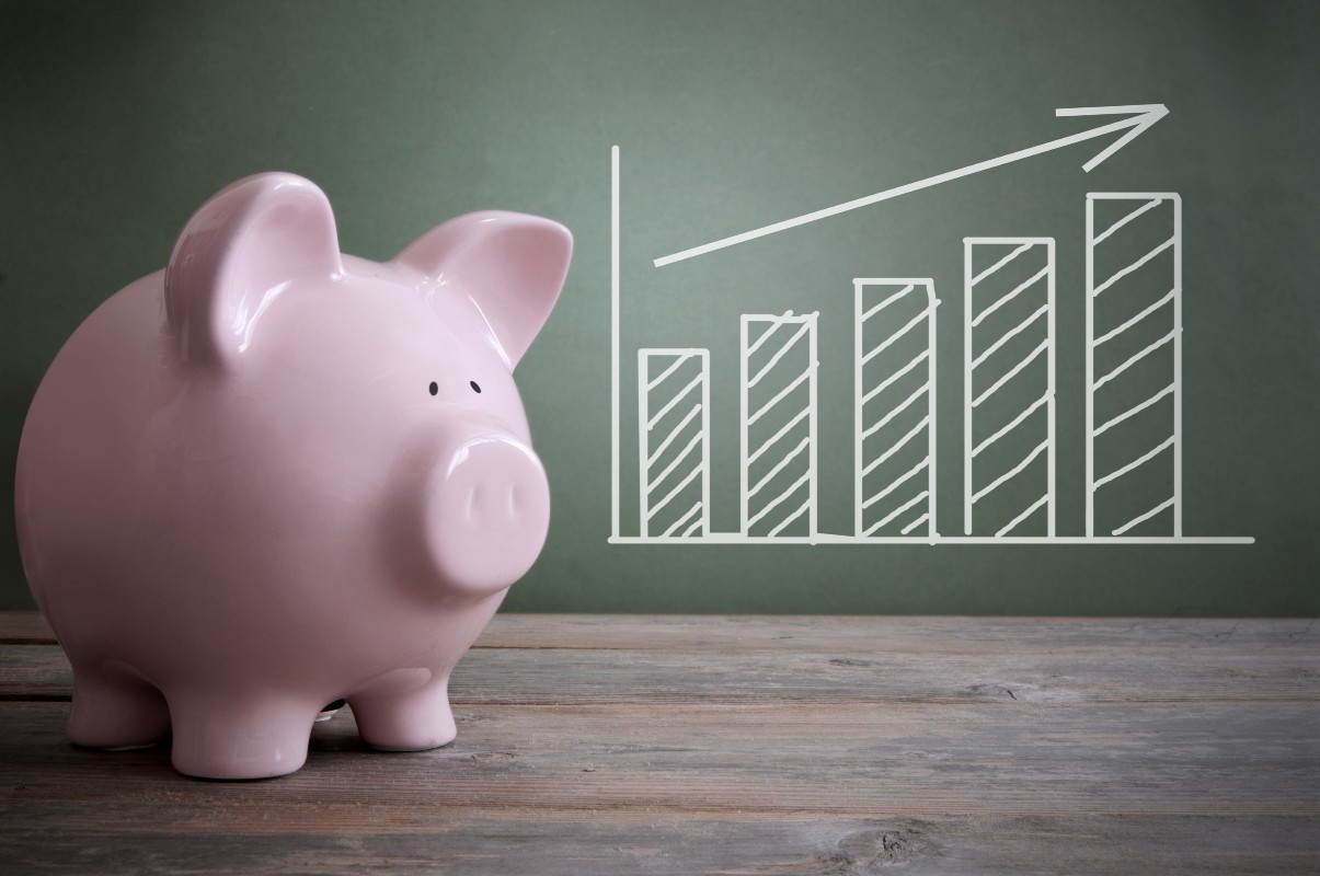 Chalk board chart with arrow pointing upwards and piggy bank in foreground.