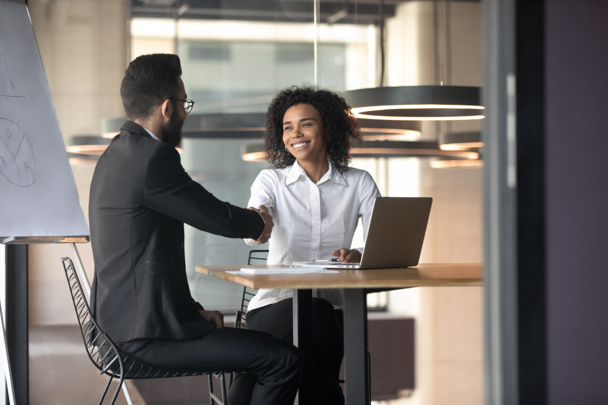 A businesswoman smiling and shaking a businessman's hand