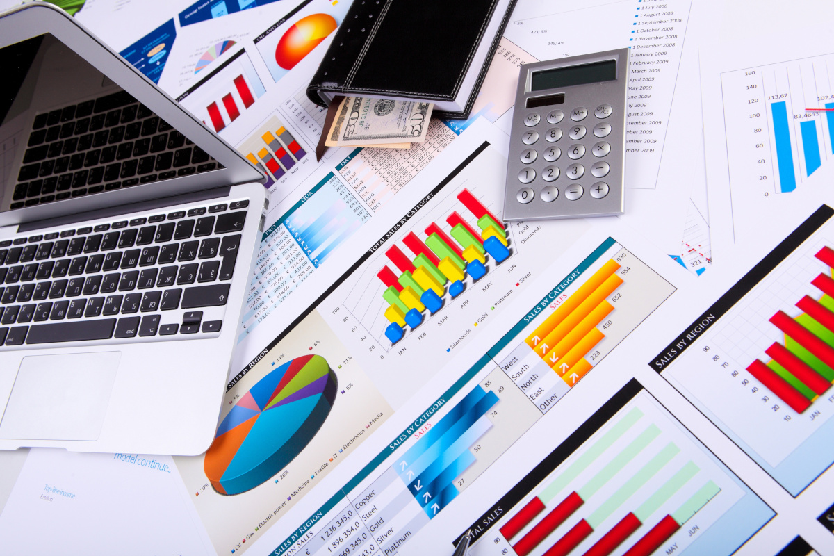 colorful graphs and charts laid out with laptop and calculator on top.