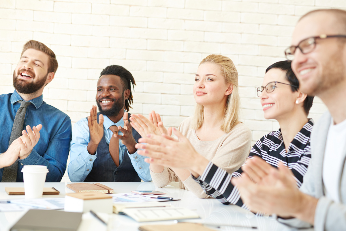 Coworkers sitting at a table clapping after watching a presentation