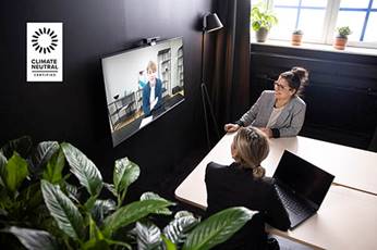 Two people video chatting with someone on a TV mounted to the wall, with a Climate Neutral Certification graphic in the top left corner of the image