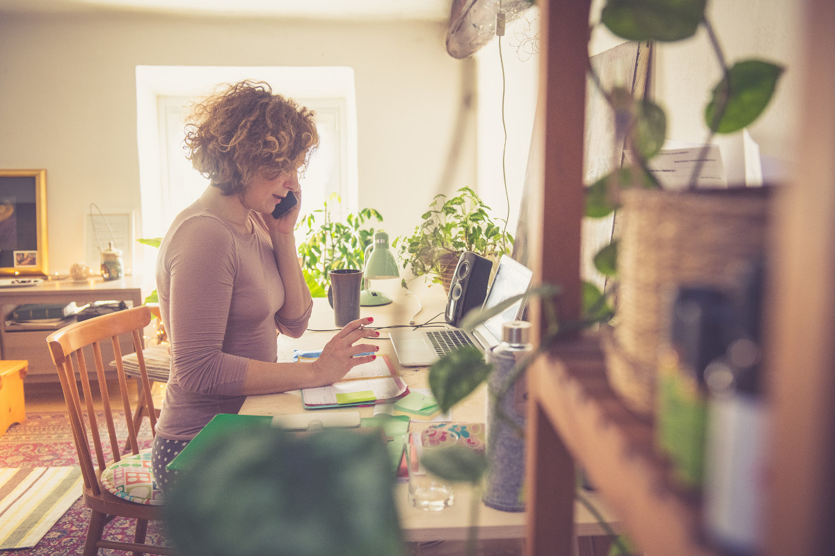 Woman working from home on her laptop, at a wooden table with green plants all around
