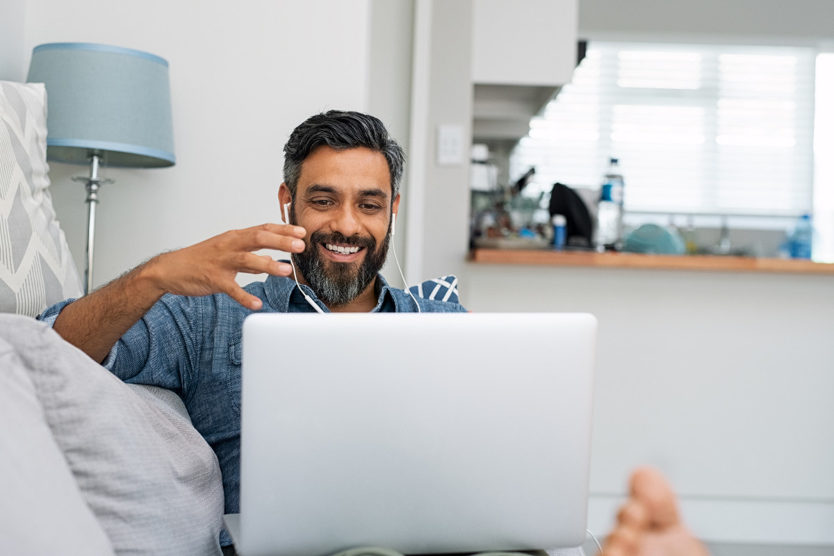 Remote worker sitting on couch at home, using VoIP technology to communicate through his laptop
